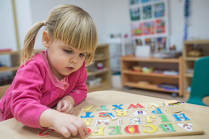 Little girl playing with wooden puzzle at a Preschool & Daycare Serving Brighton, MI